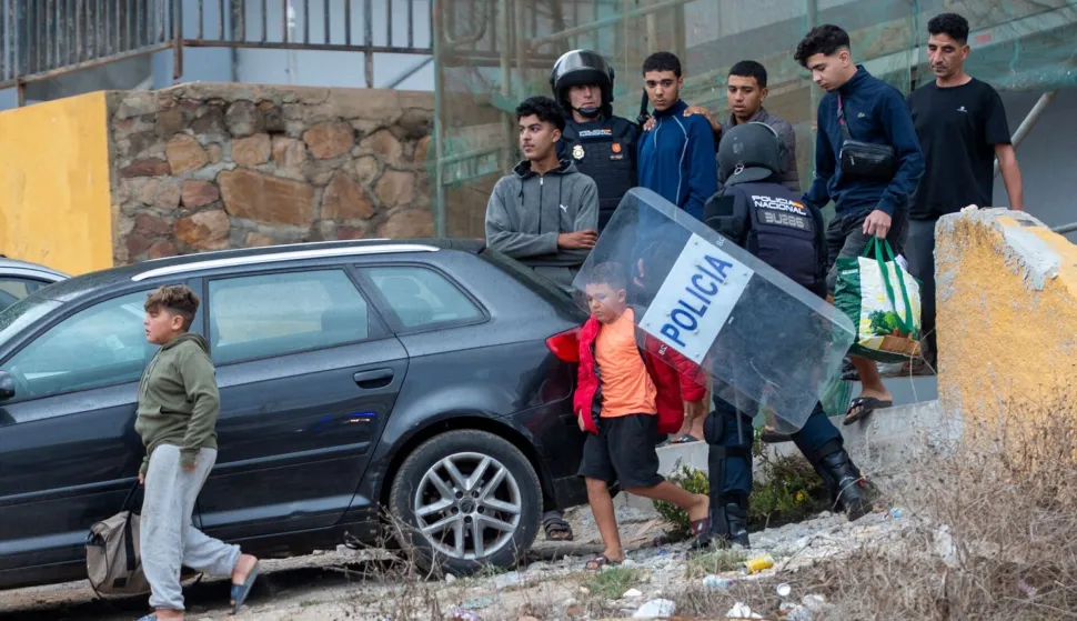 Migrants, including at least two minors, carry their belongings as Spanish police round up migrants sleeping rough outside the Tarajal warehouses on the outskirts of Spain's north African enclave of Ceuta on October 18, 2026. Scores of migrants remain sleeping rough in outlying neighborhoods of the city since the massive influx of tens of thousands of migrants from Morocco in late July, fueling tension in this Spanish North African enclave of some 80,000 inhabitants. Migrants are being transported by bus to police facilities, with minors taken to the National Police headquarters and adults transferred to the Tarajal Temporary Assistance Centre for Foreigners (CATE) for identification, registration and screening. (Photo by Antonio Sempere/AFP)