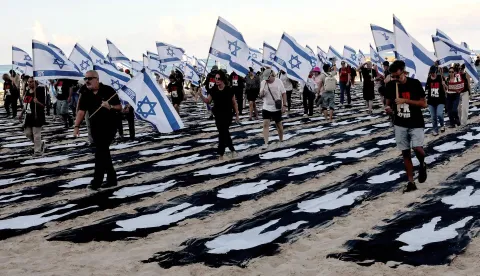 TOPSHOT - People carrying Israeli flags walk through a commemorative installation set up on the beach in Tel Aviv to mark the third anniversary of Hamas's October 7 attack on Israel, on October 7, 2026. Israel marked the third anniversary of Hamas's October 7 attack with silent tributes, new strikes on Gaza and intense political debate, weeks before elections in which the country's deadliest day will be front and centre. (Photo by Jack GUEZ/AFP)