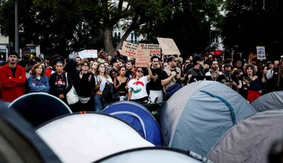 Demonstrators stand next to tents set up to protest against housing shortage, soaring rents and low wages in central Lisbon on October 17, 2026. Thousands of people marched on October 17, 2026 through the centre of Lisbon at the call of the CGTP trade union to protest against increasingly difficult living conditions. The slogans and demands focus mainly on higher wages and pensions, as well as protests against the rising cost of housing and fuel. (Photo by Filipe AMORIM/AFP)
