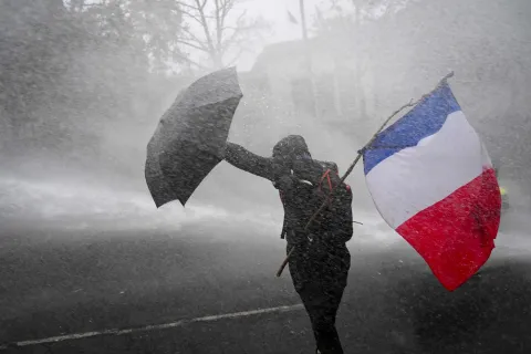 TOPSHOT - A protester holds the French flag as he protects himself from a water cannon during a demonstration in favor of purchasing power, the protection of public services, and fiscal and social justice, in Paris on October 24, 2026 as part of a nationwide call for mobilisation bringing together former members of the Yellow Vest movement, labor unions, high school and university students. Protests by high school students over learning conditions sparked a movement that has since spread nationwide, fuelled by broader anger over the rising cost of living. About 70,000 security personnel will be deployed on October 24, 2026, Interior Minister said at a news conference, warning that calls for violence and looting were circulating on social media. (Photo by Aris MESSINIS/AFP)